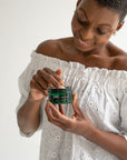 Woman holding a jar of Maslak skincare product against a white background